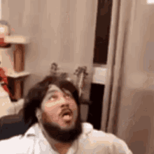 a man with a beard is wearing a wig and making a funny face in a room .