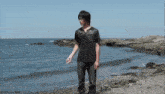 a man in a black shirt is standing on a beach next to the ocean .