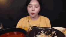 a woman in a yellow shirt is eating a bowl of food .