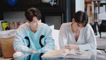 two men are sitting at a table reading a book and the word mint is on the wall