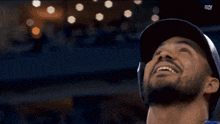 a man with a beard wearing a baseball cap with the letters sn on the bottom