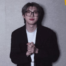 a man wearing glasses and a black jacket has his hands folded in front of him