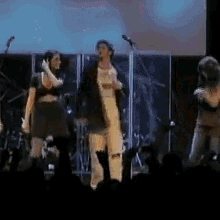 a group of people are standing on a stage singing into microphones in front of a crowd