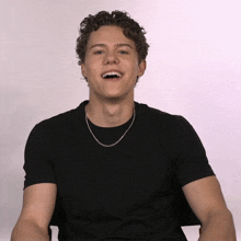 a young man with curly hair is wearing a black shirt and a silver chain necklace