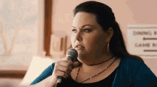 a woman is singing into a microphone while sitting in front of a sign that says game room .