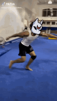 a man in a white tank top and black shorts is doing a trick on a blue mat