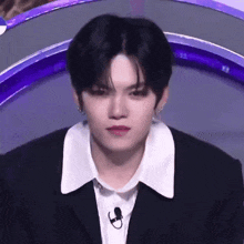 a young man in a suit and white shirt is sitting in front of a microphone on a stage .