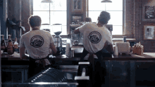 two men behind a counter wearing shirts that say ' brookstone coffee ' on them