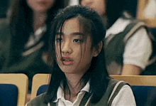 a girl in a school uniform is sitting in a classroom with other students .
