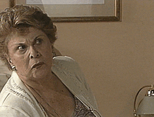 an elderly woman wearing a white sweater is sitting in a chair and looking at the camera