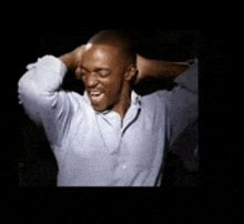 a man in a blue shirt is holding his hands behind his head .