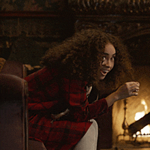 a woman with curly hair is sitting in front of a fireplace and smiling