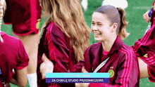 a group of female soccer players are hugging and smiling with a blue banner that says za chwile studio przemeczowe
