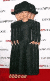 a woman in a black dress and hat is standing on a red carpet in front of a wall that says emporio armani