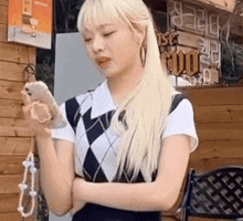 a woman with blonde hair is standing in front of a wooden building holding a phone .