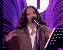 a woman in a suit is singing into a microphone while holding a music stand .