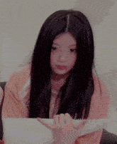 a girl with long black hair is sitting on a couch holding a piece of paper in her hand .