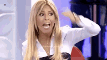 a woman with blonde hair and a white shirt is making a funny face while holding her hand to her head