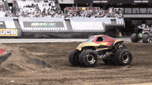 two monster trucks are racing on a dirt track in front of a jcb sign