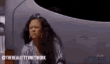 a woman is sitting in front of a silver car and making a funny face .