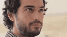 a man with a beard and curly hair is looking at the camera .