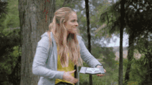 a woman is standing in the woods holding a remote control in her hand .