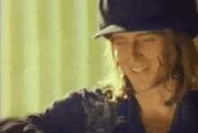 a man with long hair and a hat is smiling .