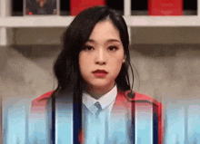 a woman in a red jacket and tie is standing in front of a microphone and looking at the camera .