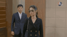 a man in a suit and a woman in sunglasses are walking in a hallway