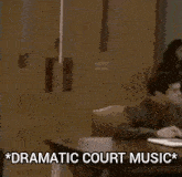 a man in a suit and tie is standing next to a man sitting at a table with dramatic court music written on it .