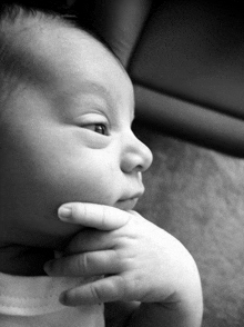 a black and white photo of a baby holding his hand to his chin