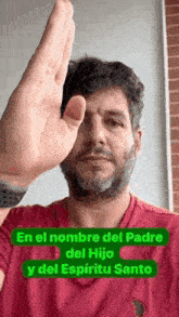 a man with a beard and a red shirt is holding his hand up to his face .