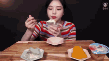 a woman is sitting at a table eating a dessert with a spoon
