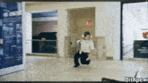 a man in a white shirt and black pants is running in a hallway with a sign that says exit on it