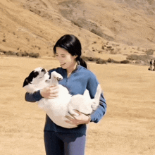 a woman in a blue jacket is holding a small white dog