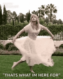 a woman in a white dress is dancing in the grass with the words `` thats what im here for '' .