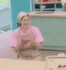 a blurry picture of a woman in a pink apron standing in a kitchen .