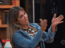 a woman in a denim jacket is making a funny face with her hands in the air