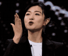 a woman in a suit and white shirt is making a funny face while raising her hand in the air .