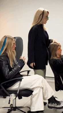 a woman wearing a black jacket and white pants sits in a chair