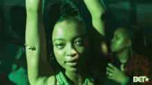 a woman in a green dress is dancing with her arms in the air and a bet logo in the background
