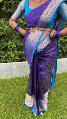 a woman wearing a blue blouse and a blue saree is standing in the grass .