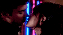 a man and woman are kissing in front of a neon sign