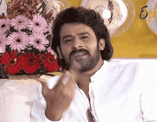 a man with a beard is sitting in front of a bouquet of flowers and balloons .