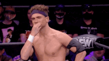 a shirtless wrestler wearing a purple headband is standing in a ring covering his mouth with his hand .