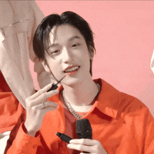 a young man in a red shirt is holding a microphone and applying lipstick