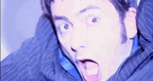a man in a blue suit and tie is making a surprised face with his mouth open .