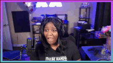 a woman wearing headphones and a shirt that says `` these hands '' is sitting in front of a microphone
