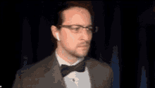 a man with glasses and a bow tie is adjusting his tie