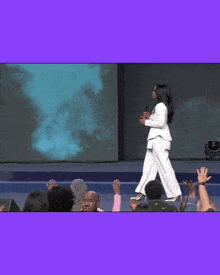 a woman in a white top stands in front of a purple background